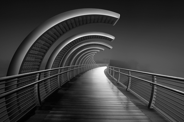 Exquisite black-and-white fine art image portraying a pedestrian bridge in Abu Dhabi amid misty weather, highlighting its prominent leading lines.