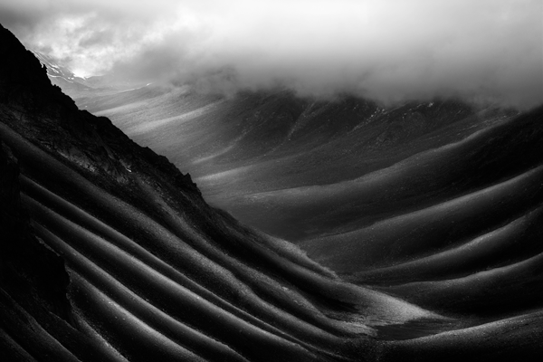 Fine art black and white photograph showcasing the breathtaking landscape of Ladakh, featuring layered valley walls illuminated by light under a foggy sky.