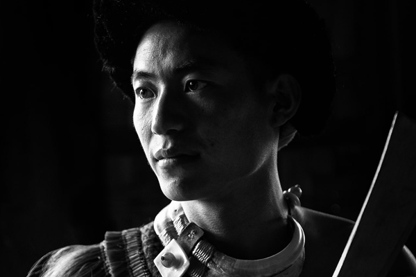 An intimate black and white portrayal featuring an Angami tribesman from Nagaland, India, clad in customary garments, captured up close.