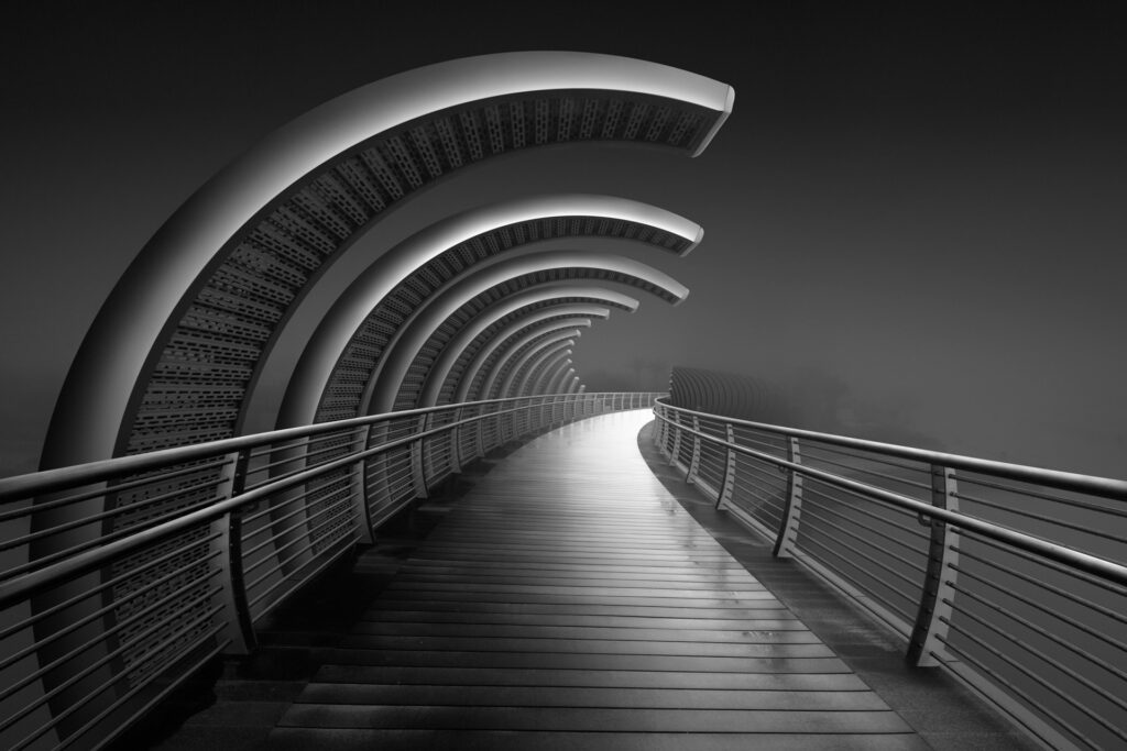 Black and white fine art photograph of a pedestrian bridge in Abu Dhabi on a foggy day, showcasing leading lines.